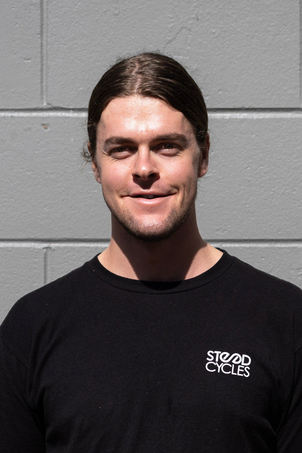 Person wearing a black t-shirt with a logo against a gray brick wall