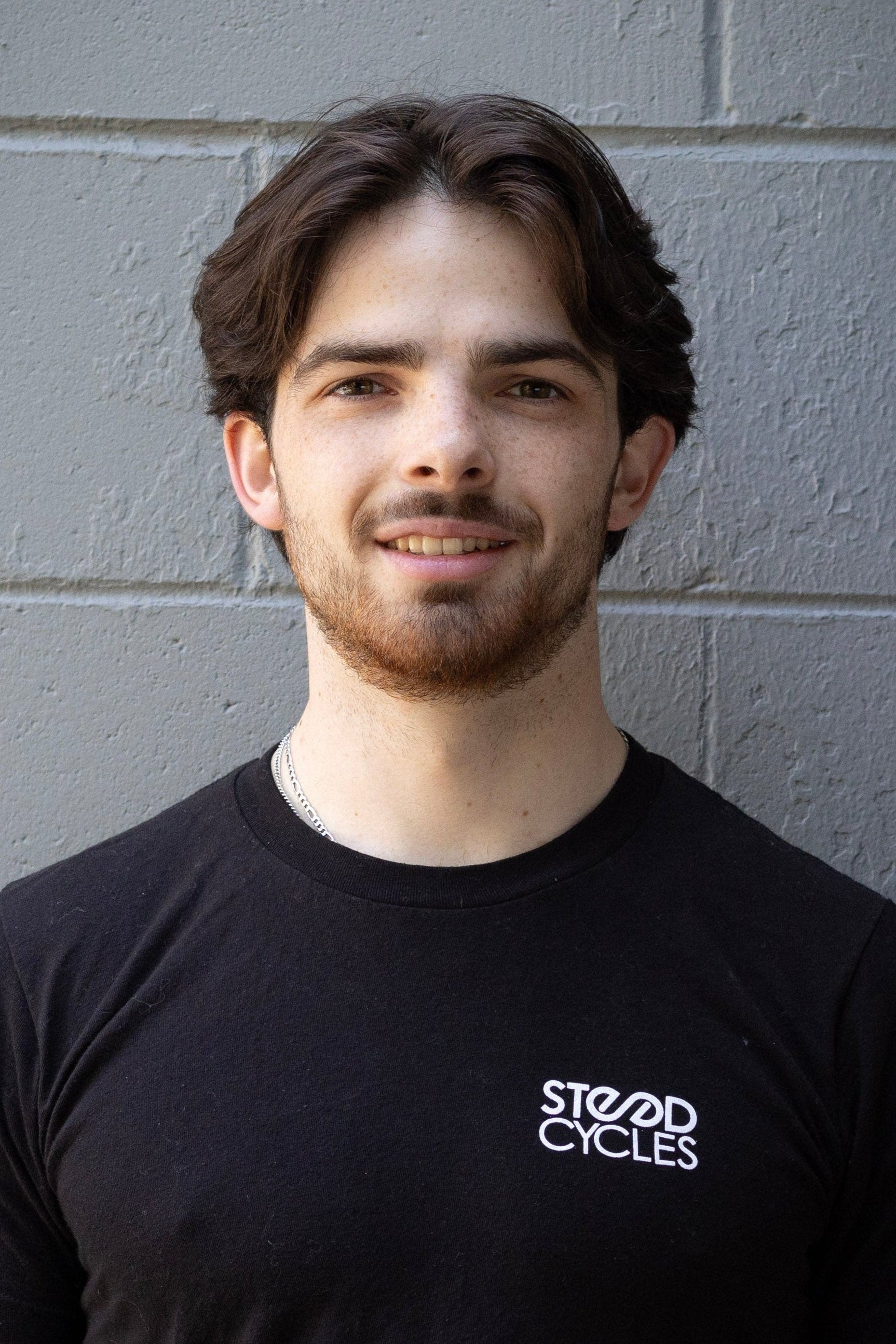 Staff member wearing a black t-shirt with 'Steed Cycles' logo against a gray brick wall