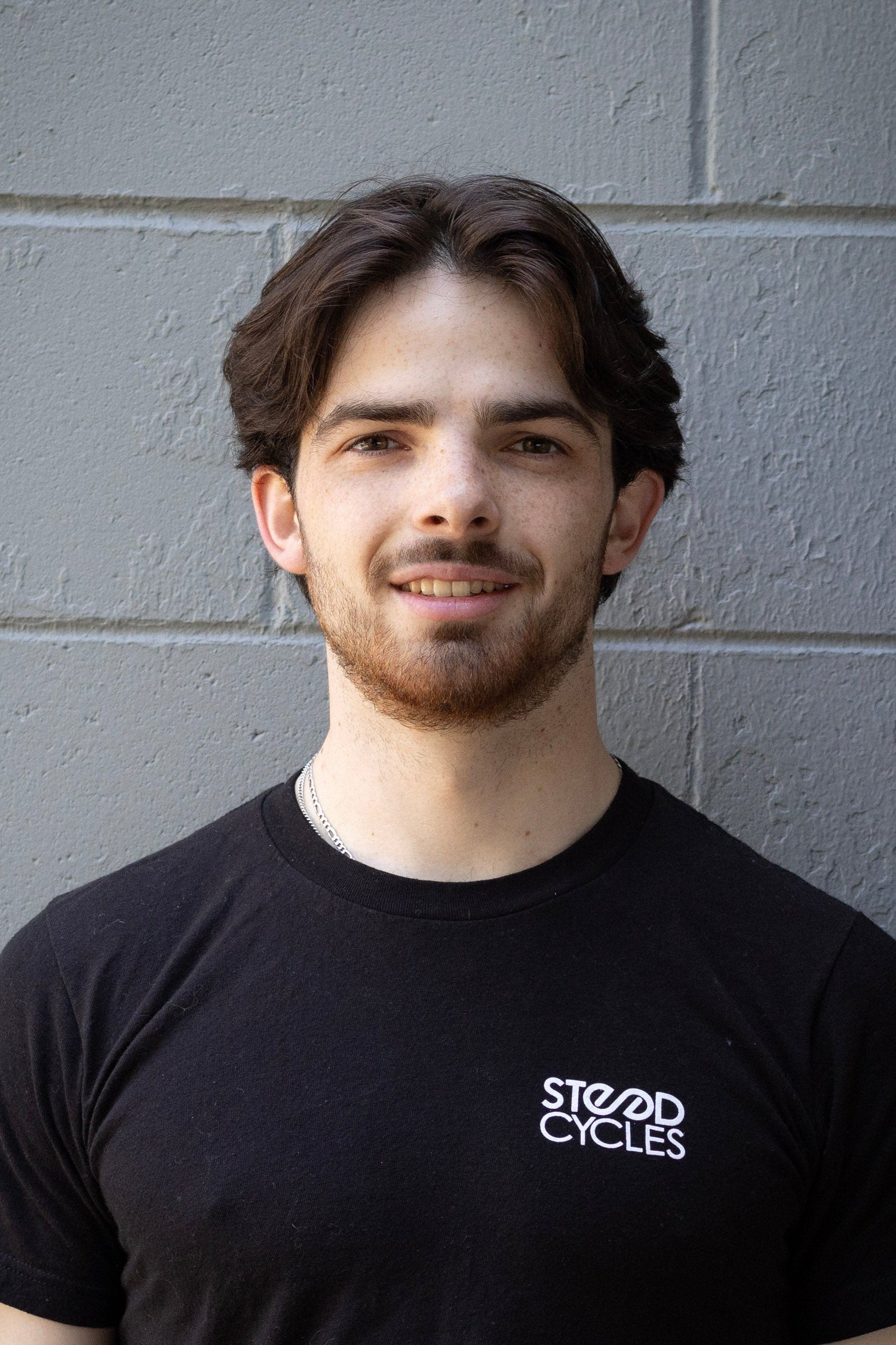 Staff member wearing a black t-shirt with 'Steed Cycles' logo against a gray brick wall